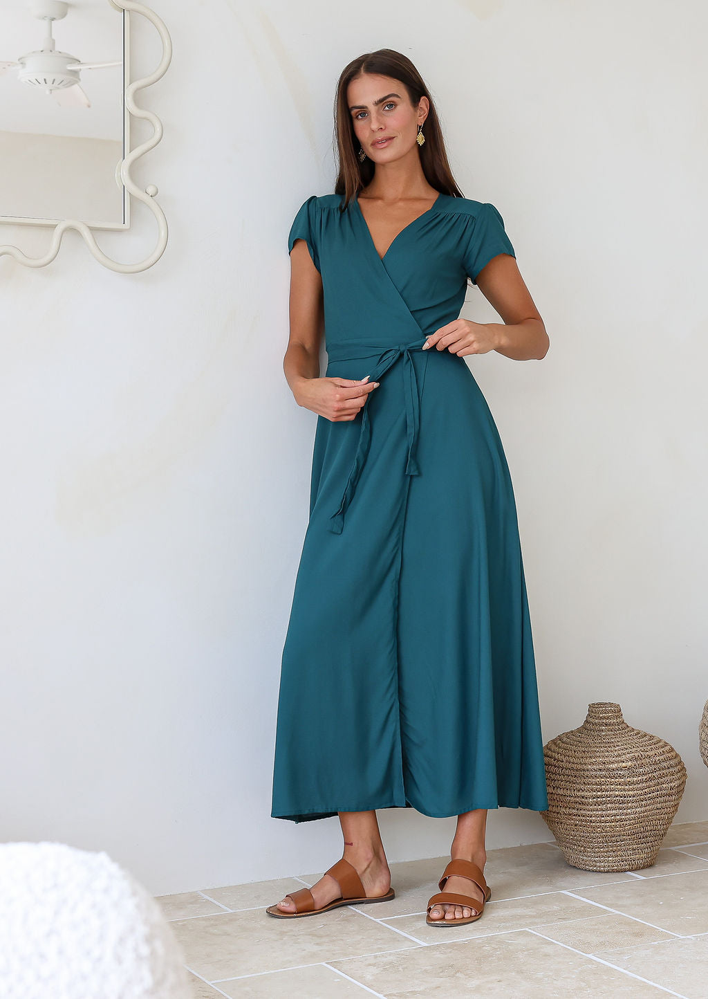 Woman wearing a teal rayon wrap dress holding the bow that is tied at the front
