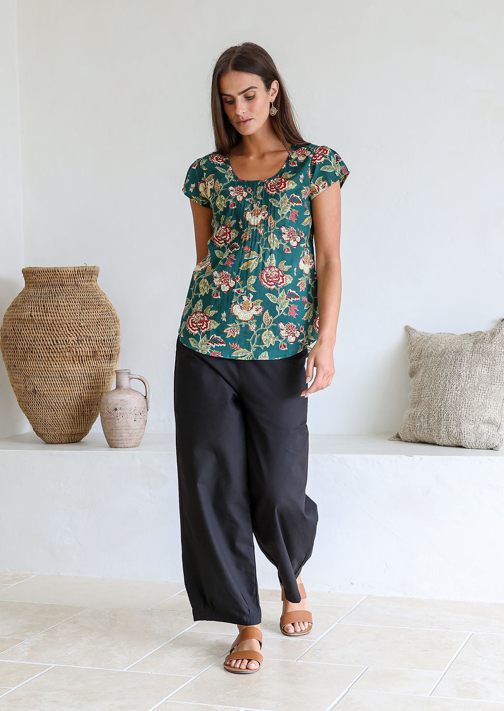 Woman wearing a bottle green based floral print short sleeve top with scoop round neckline and pleated detail across the bodice