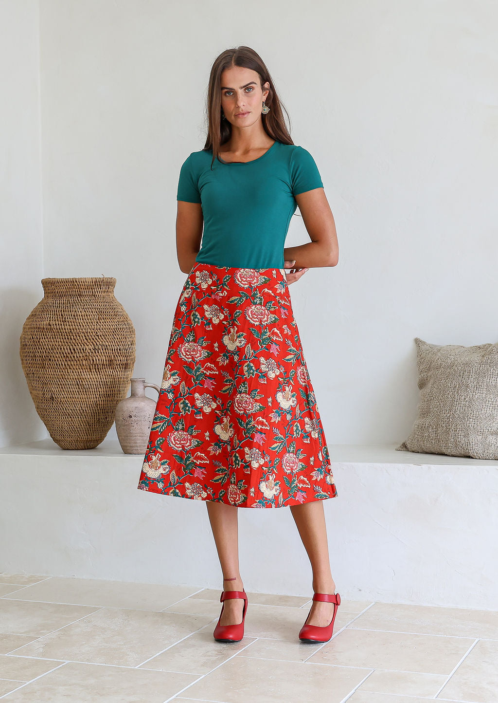 Woman wearing a green top and red floral cotton skirt in a room with decorative vases.