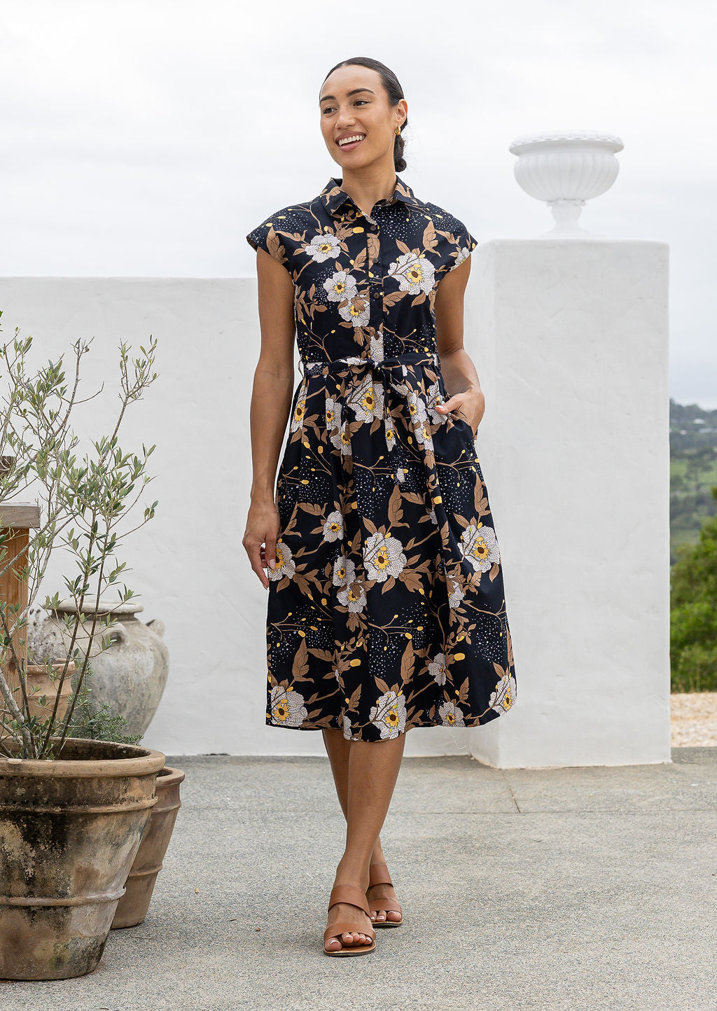 Model posing in a black floral print shirt style 100% cotton dress with cap sleeves and detachable waist tie