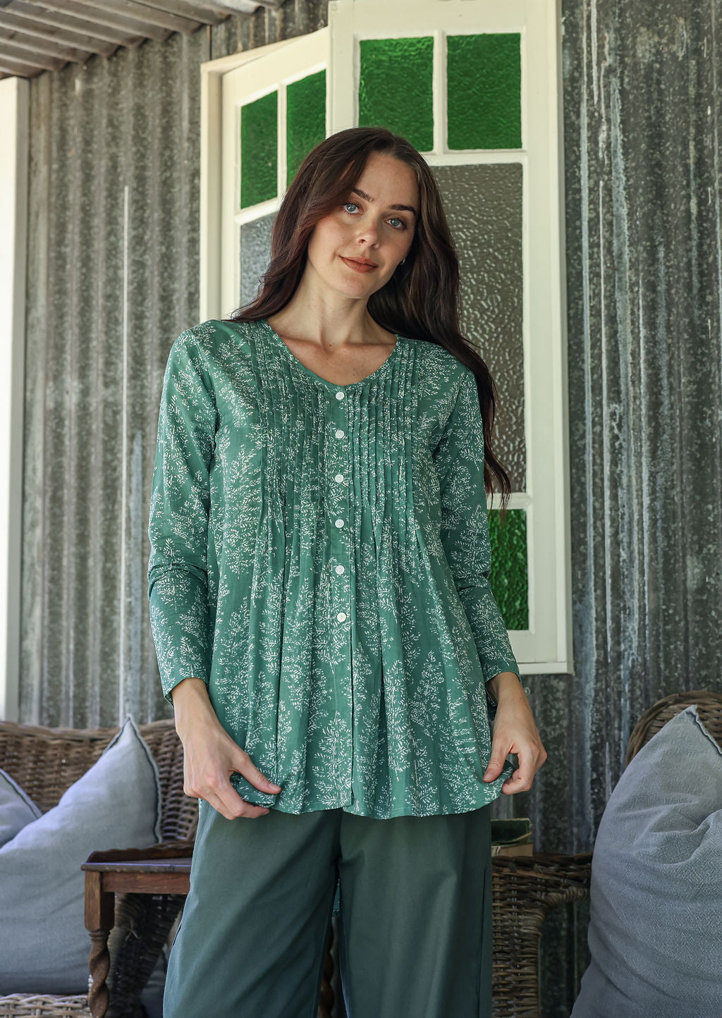 Woman wearing a sage green based cotton floral long sleeve relaxed fit blouse with a V-neckline, standing in a room
