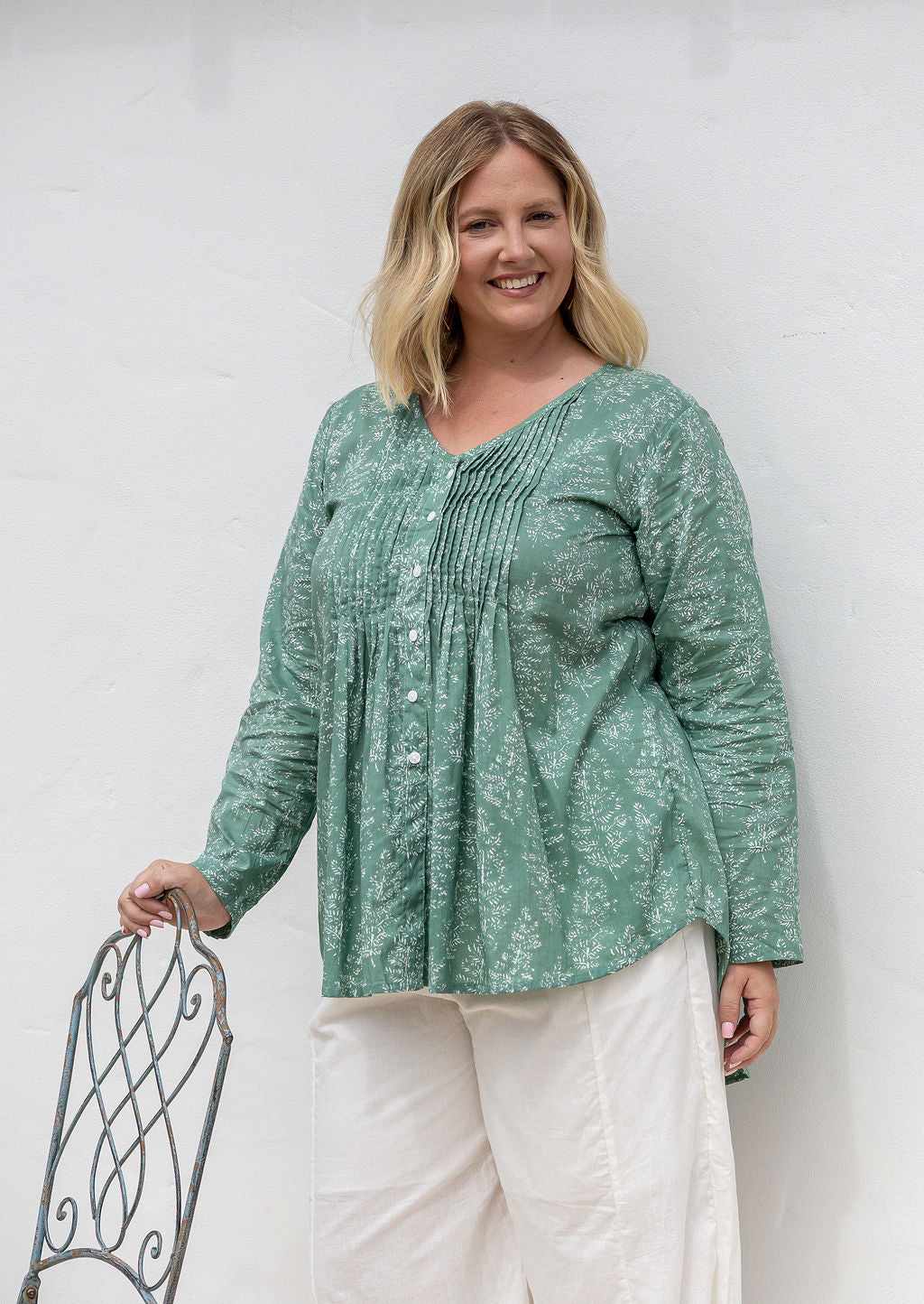 Woman wearing a sage green based cotton floral long sleeve relaxed fit blouse with a V-neckline.