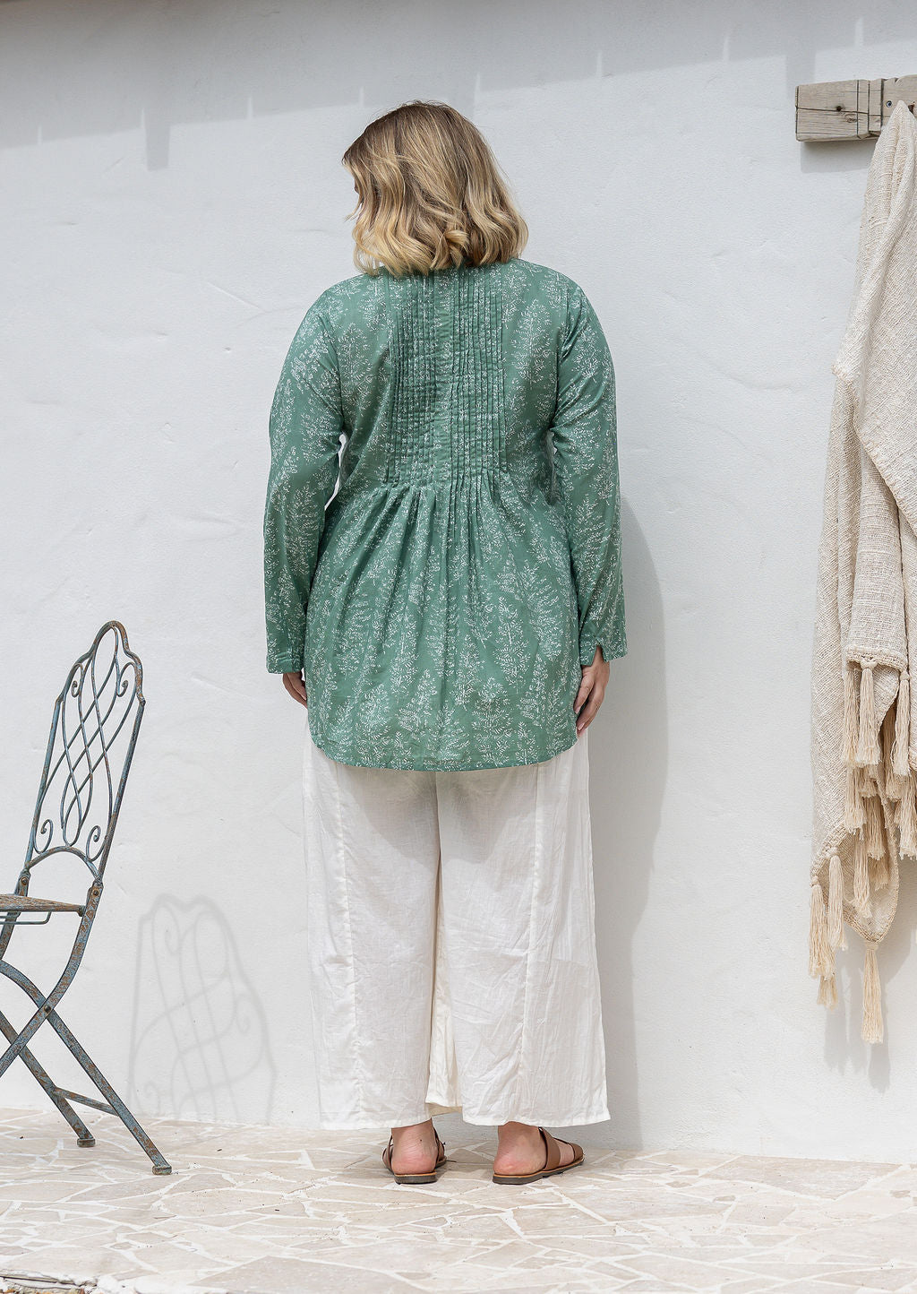 Woman stands backwards wearing a cotton long sleeve shirt that is longer at the back, paired with plain cotton pants