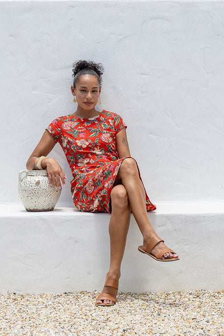 woman wearing bright red cotton floral retro style dress sitting on white wall