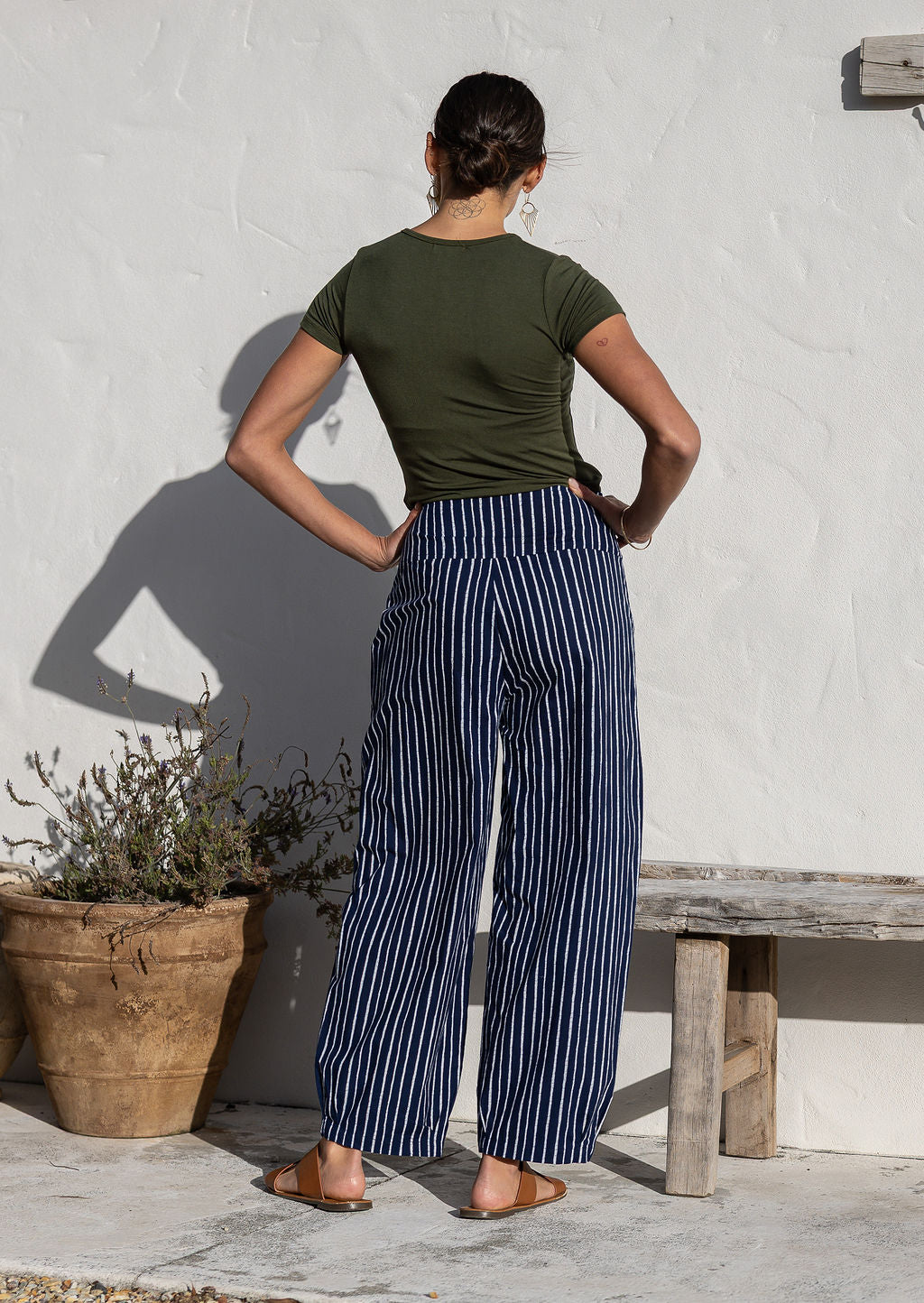 Model standing backwards wears 100% cotton wide leg pants with side zipper, pockets and small pleats at ankles.