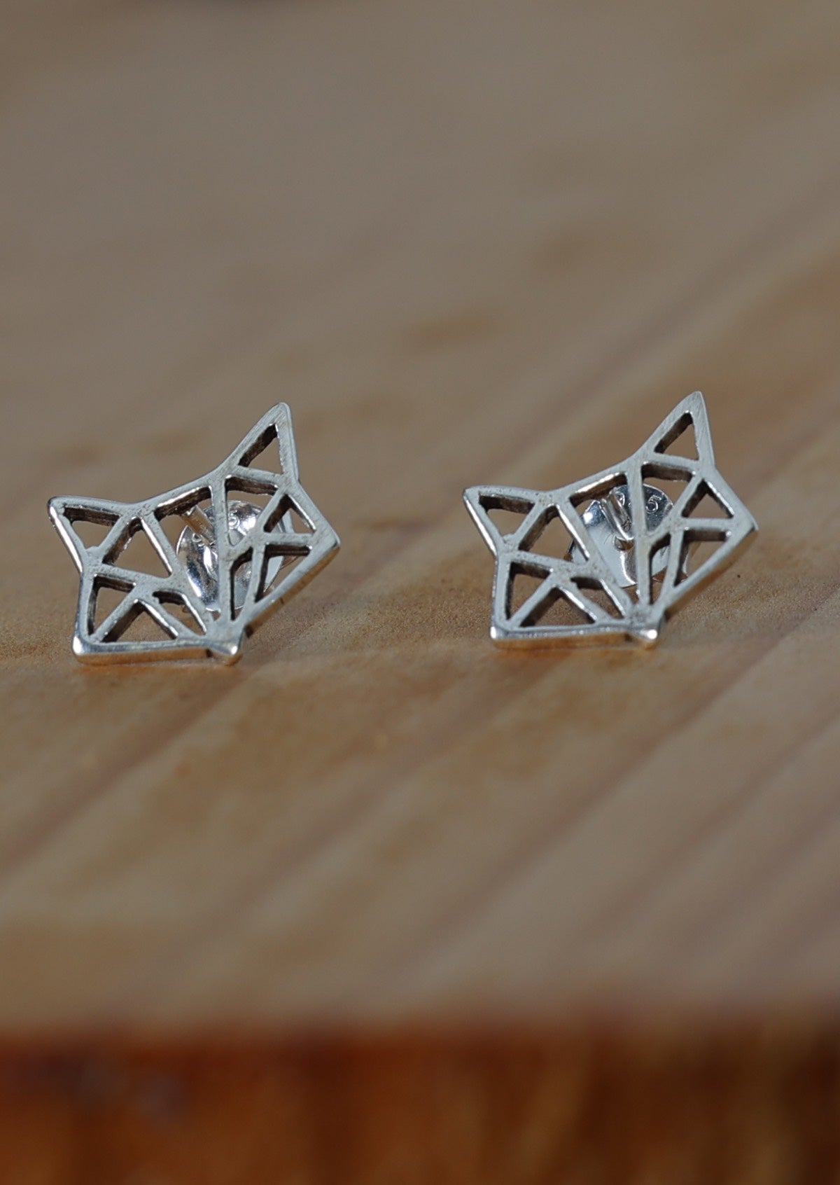 Origami Fox silver stud earrings on a wooden surface