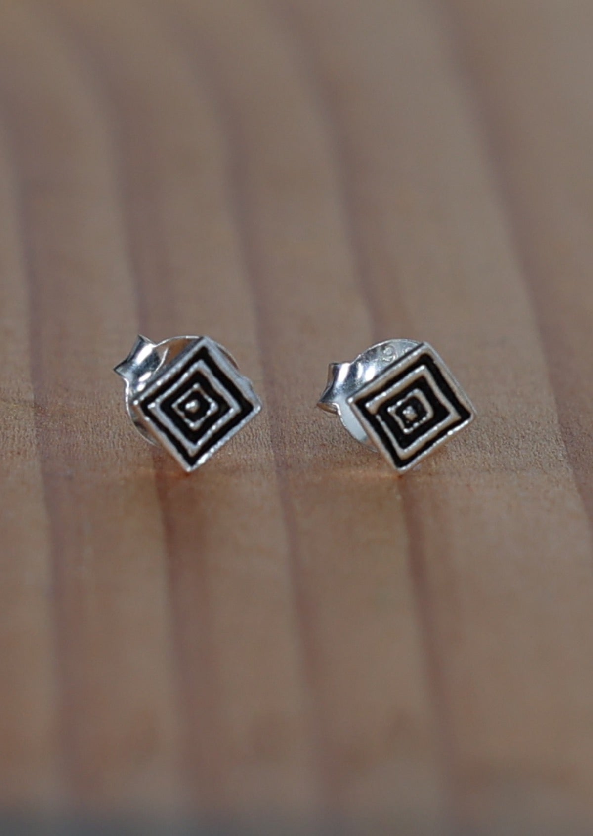 A pair of silver stud earrings with a geometric ripple design, placed on a wooden surface