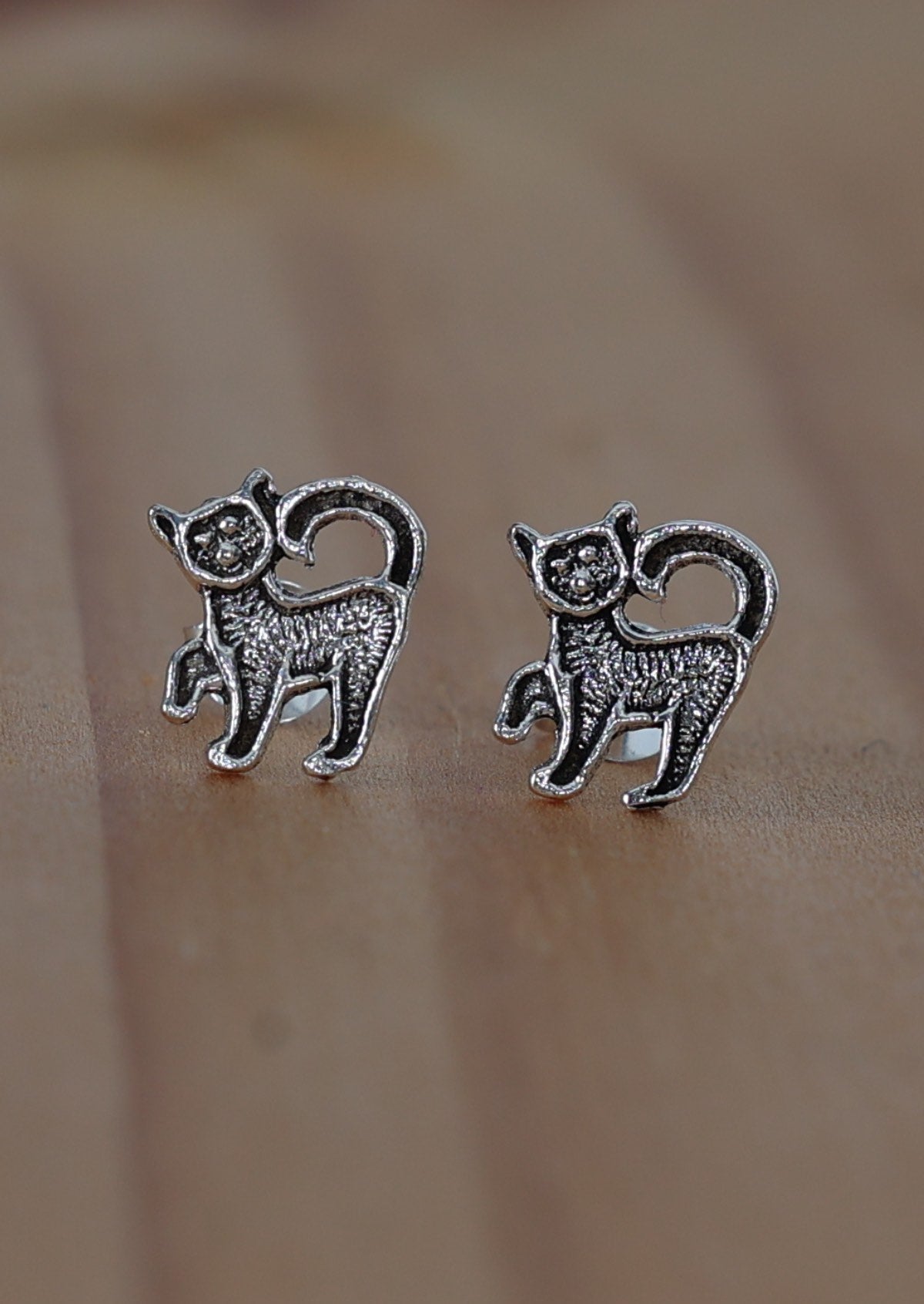 A pair of sterling silver earrings in the shape of kittens, displayed against a wooden background.