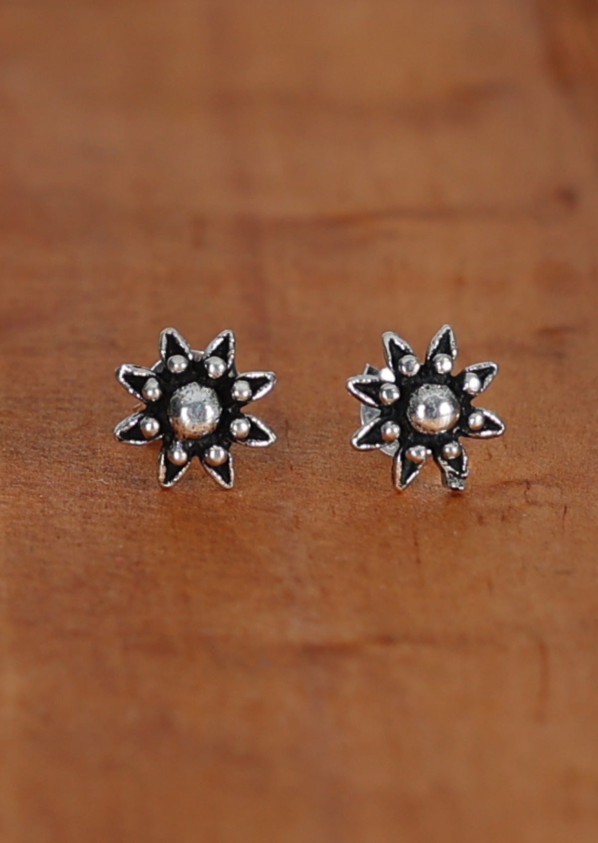 A pair of Boho Silver Flower stud earrings with intricate design, displayed against a wooden background.