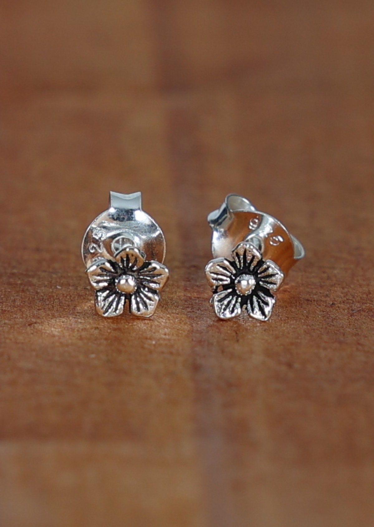 A pair of sterling silver stud earrings with a flower design, displayed on a wooden surface