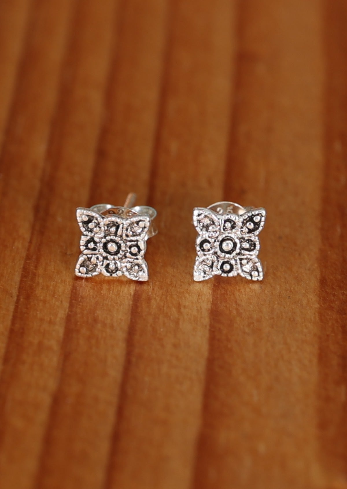A pair of Boho Bloom silver stud earrings with a floral design, displayed against a wooden background