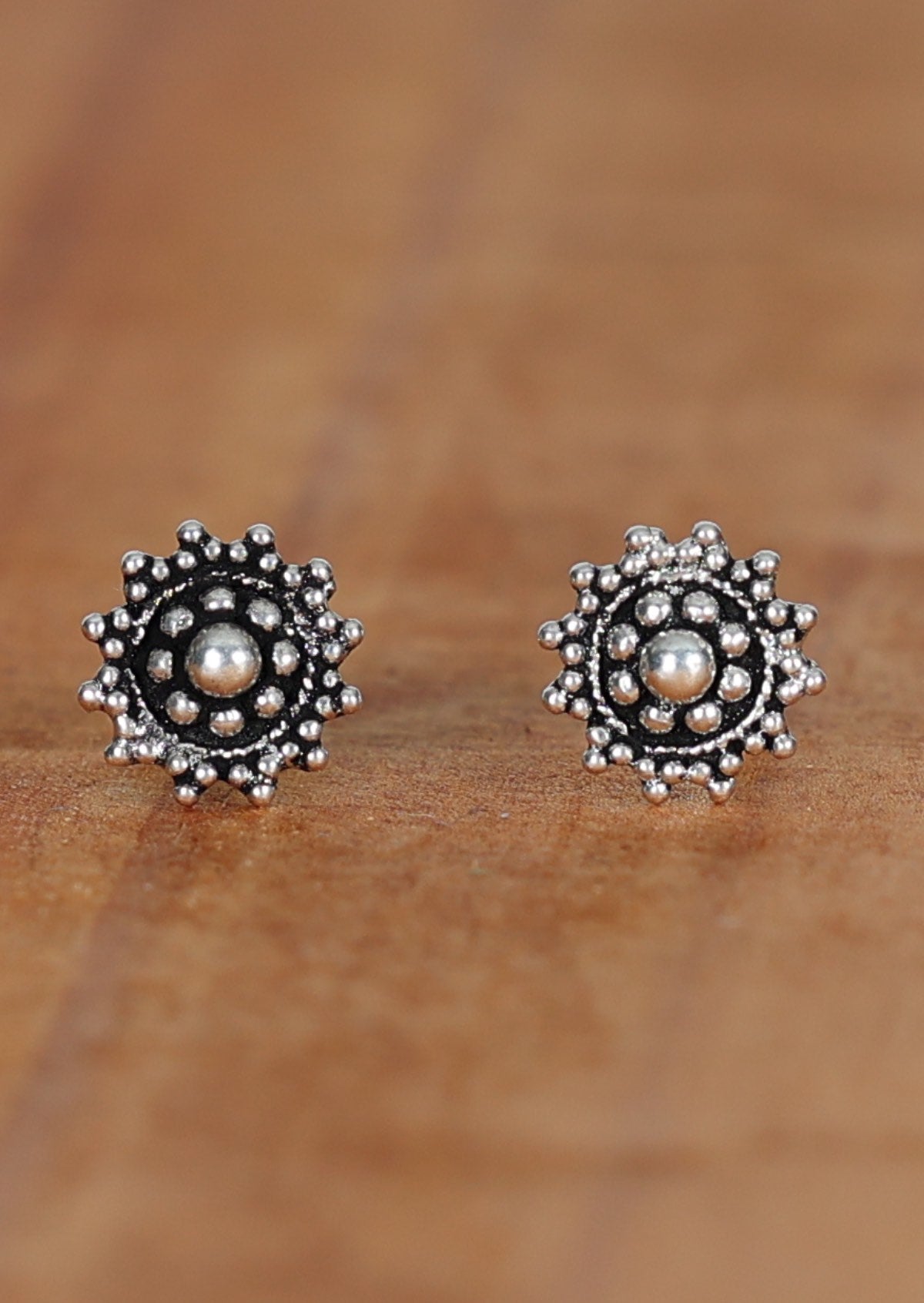 A pair of silver ornate stud earrings with intricate designs, displayed on a wooden surface.