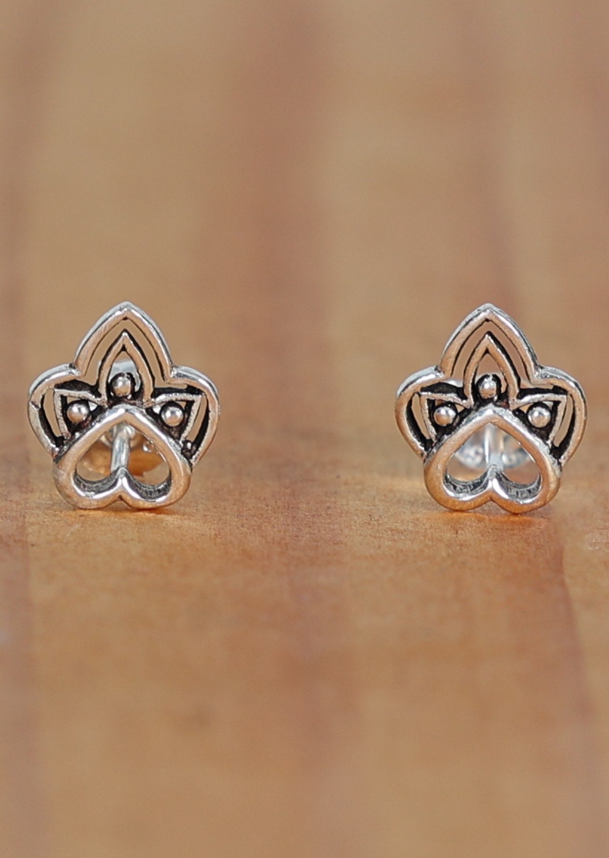 A pair of sterling silver boho heart stud earrings featuring a tribal-inspired shape within a heart outline, displayed on a wooden surface.