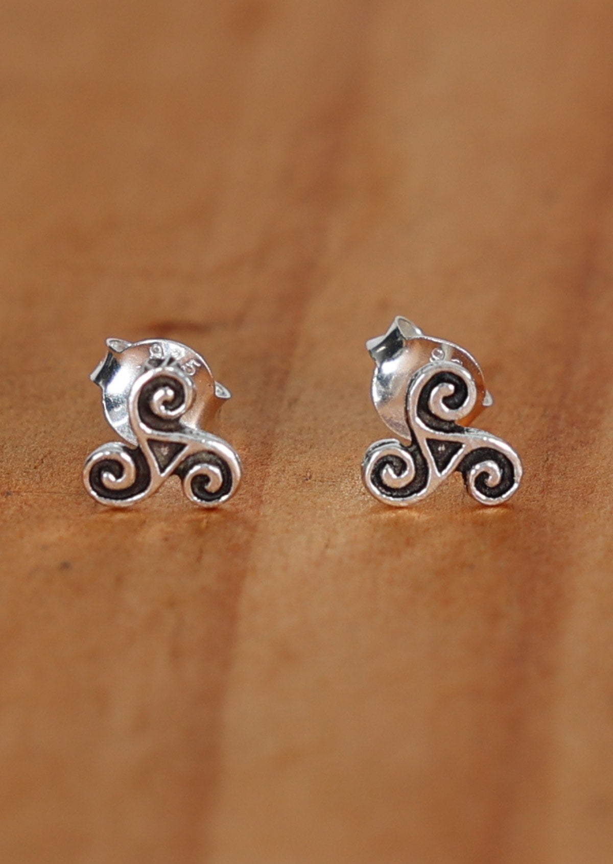 A pair of sterling silver stud earrings with a triskele design, displayed on a wooden surface
