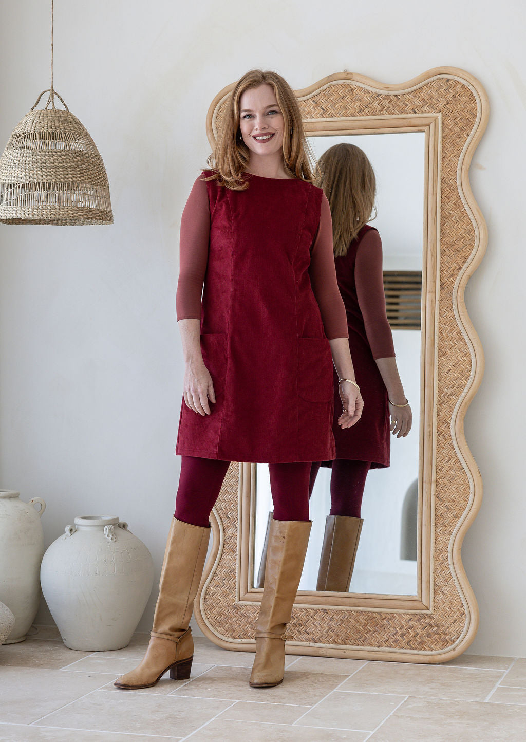 Woman poses in cotton corduroy tunic in cabernet paired with tan boots and leggings