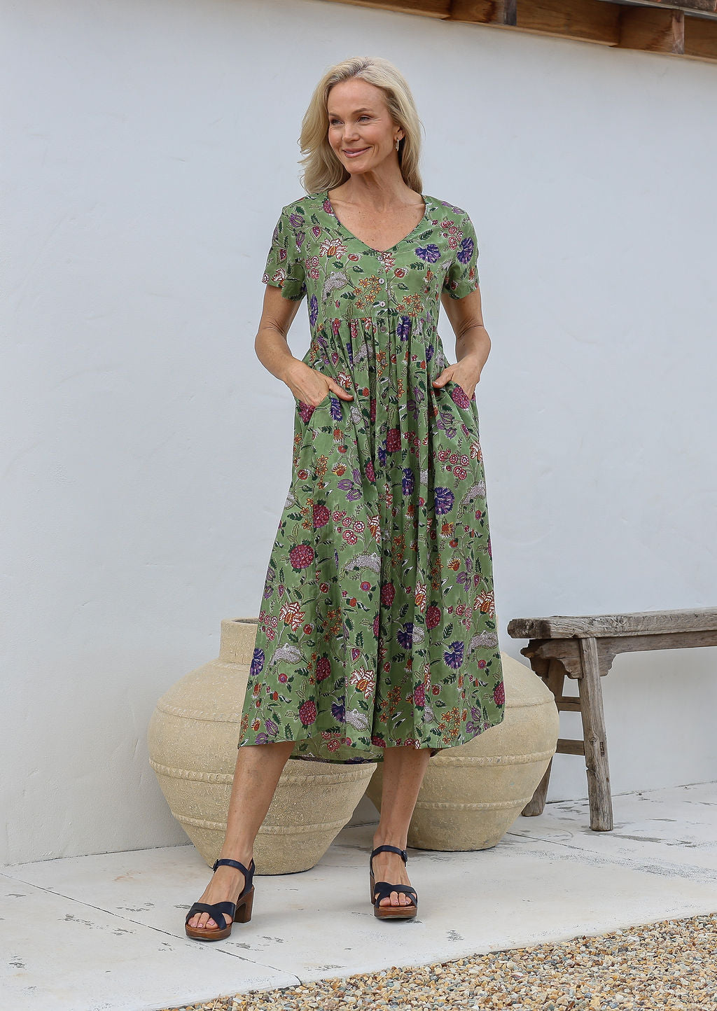 Woman standing with both the hands in pockets wearing a relaxed fit midi length cotton dress with empire waistline and gathered design.