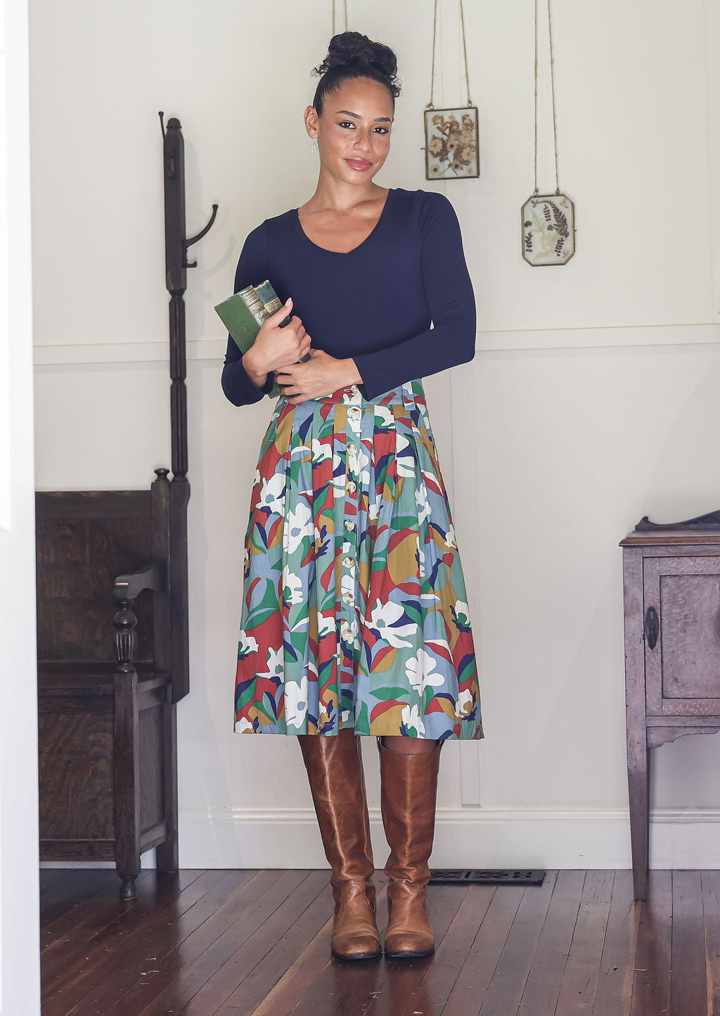 Woman wearing a navy top and colourful floral print A-line, button through cotton skirt with box pleats, belt loops and pockets