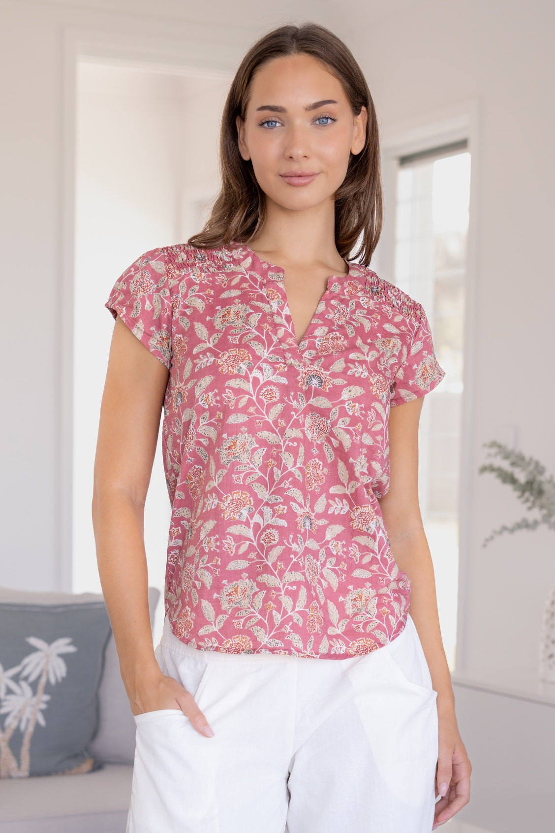 Woman wearing a 100% cotton warm pink based floral blouse and white pants.
