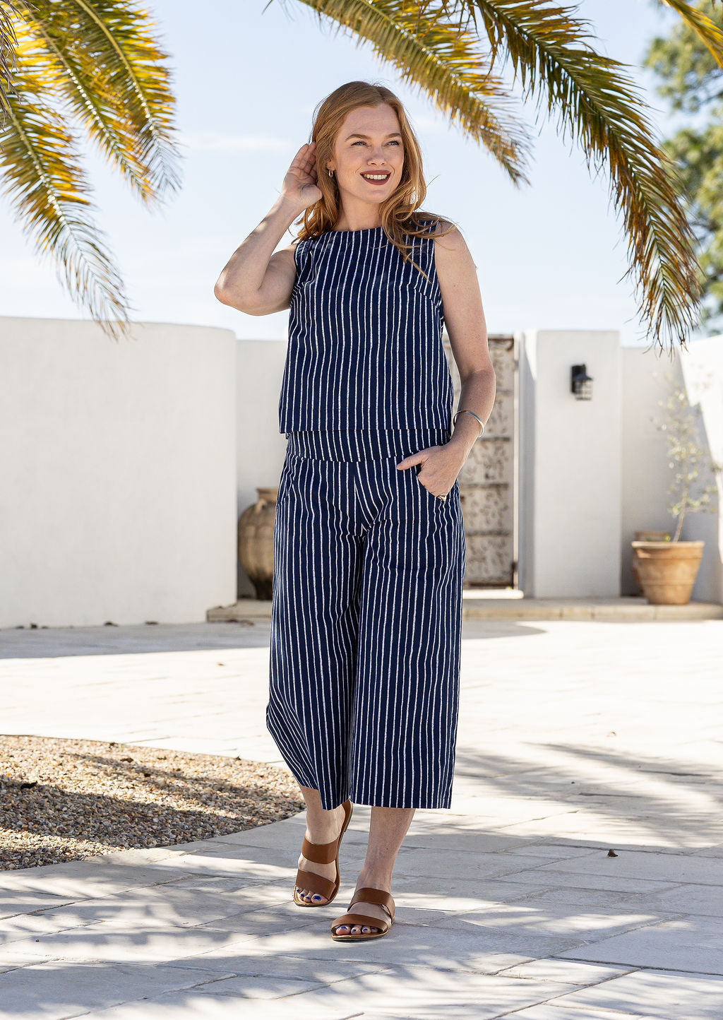 Woman wearing a navy based white striped print wide leg, 3/4 length cotton pants with side zipper