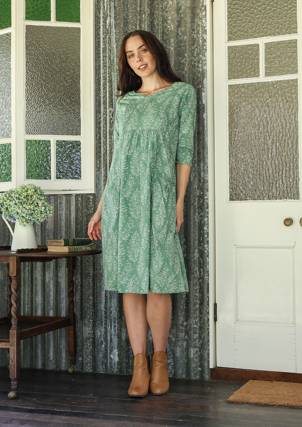 Woman poses in a 100% cotton sage green based floral dress with sleeves and pockets