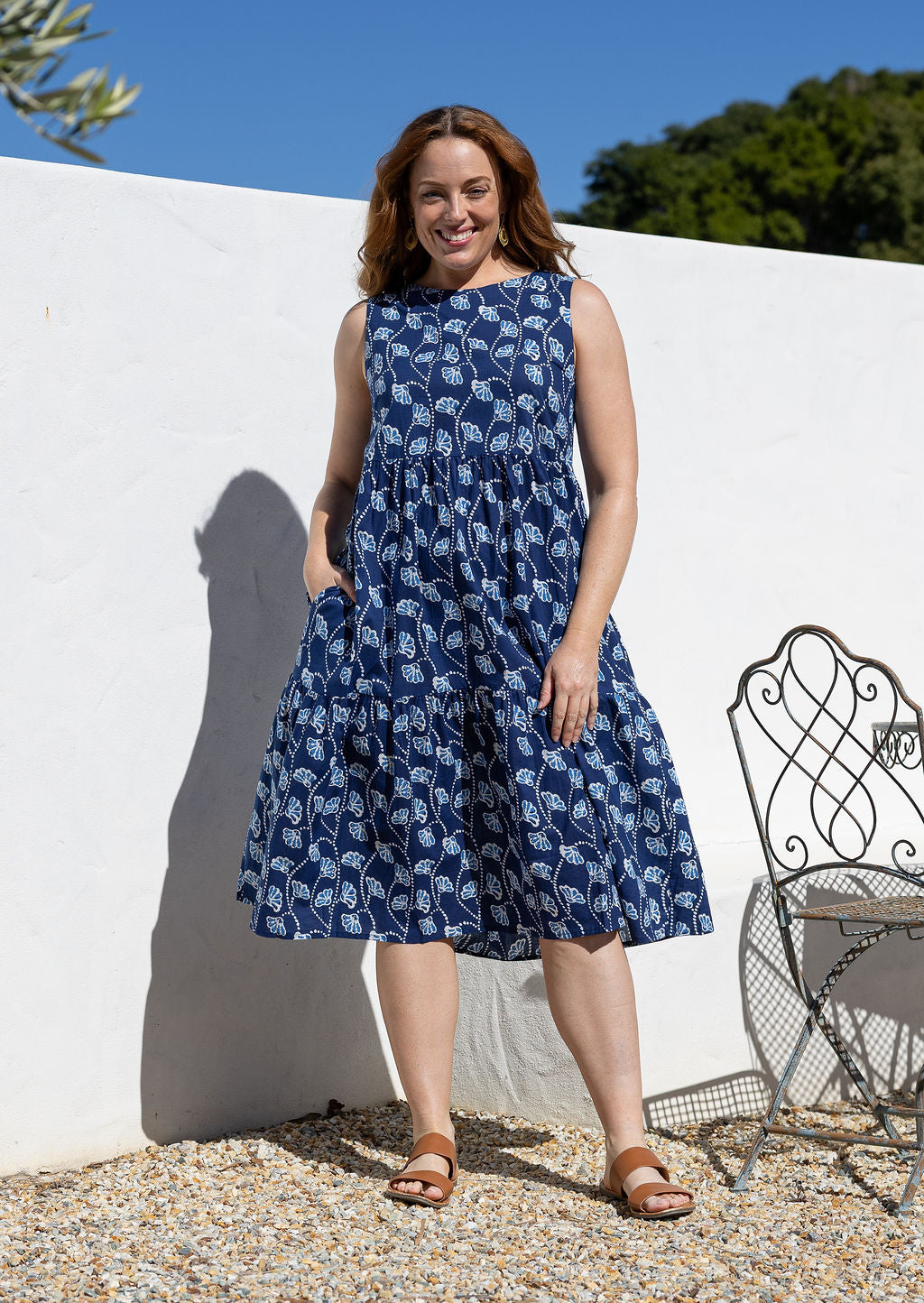 Woman wears a sleeveless, relaxed fit floral cotton dress with tiered style, empire waist and pockets.