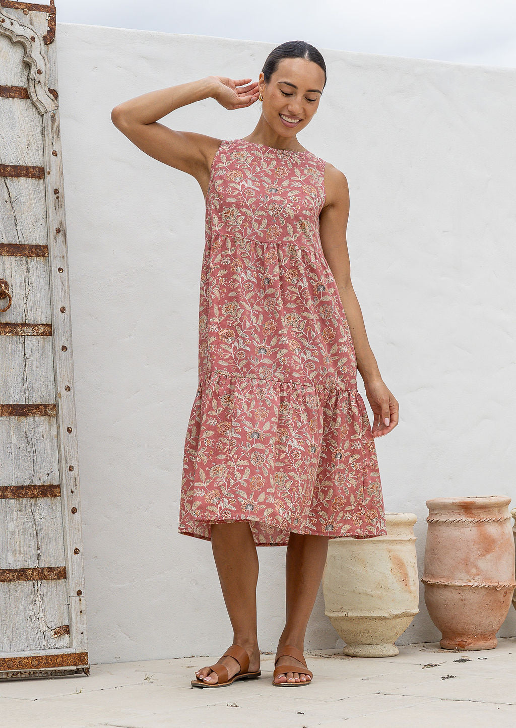 Woman wears a sleeveless, relaxed fit floral cotton dress with tiered style, empire waist and pockets.