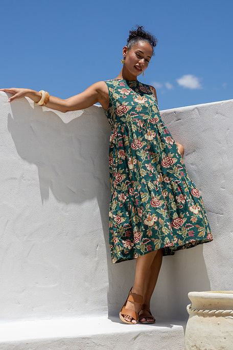 Woman in 100 percent cotton relaxed fit sleeveless dress with high round neckline, pockets and tiered style.