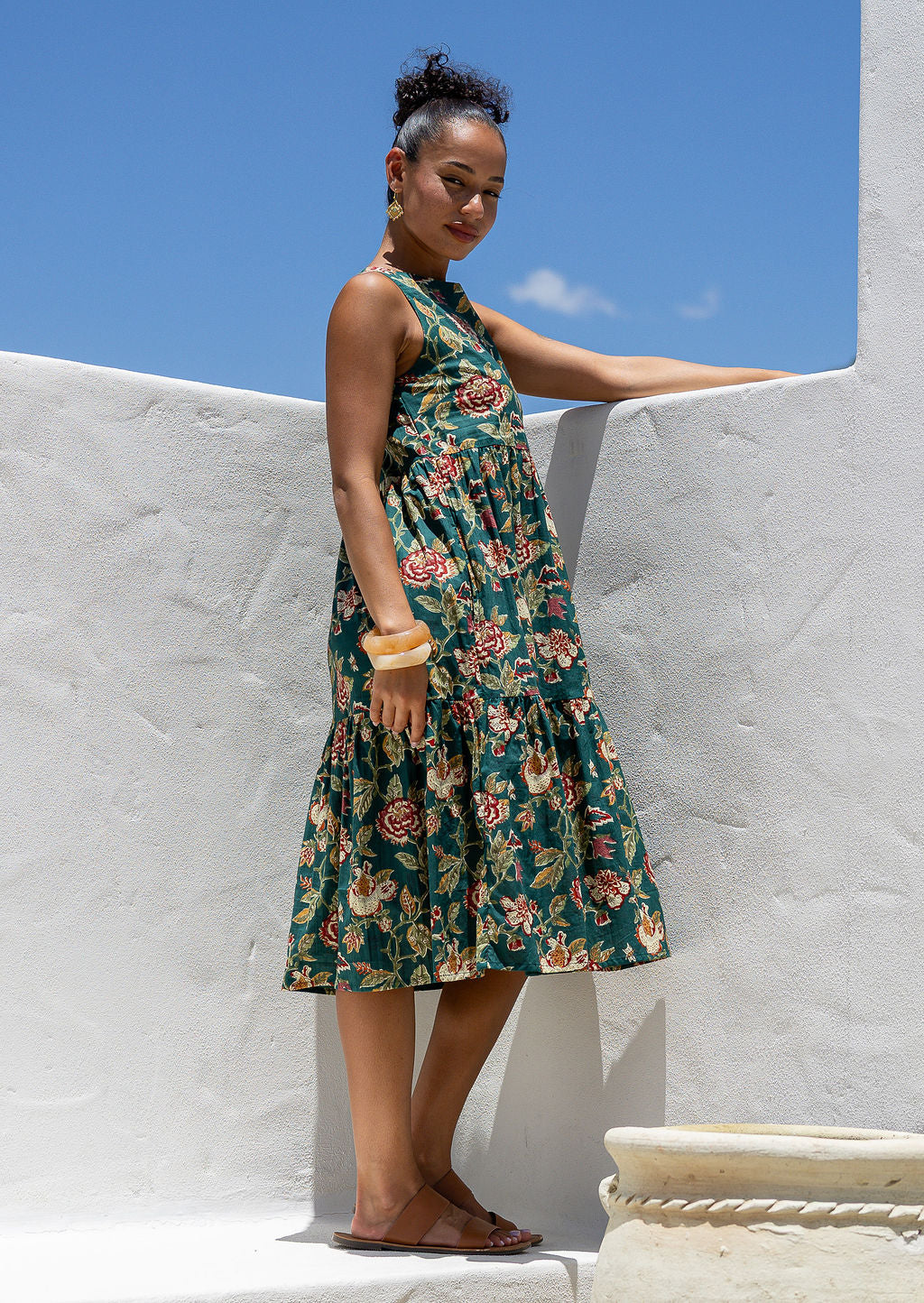 Woman wears a sleeveless, relaxed fit floral cotton dress with tiered style, empire waist and pockets.