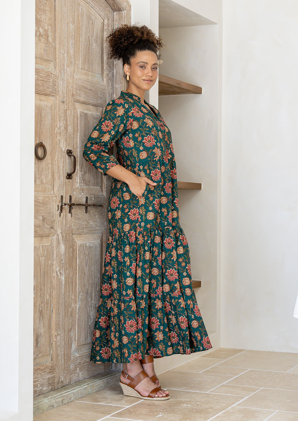 Woman wearing a green floral cotton dress with sleeves with her hands in pockets