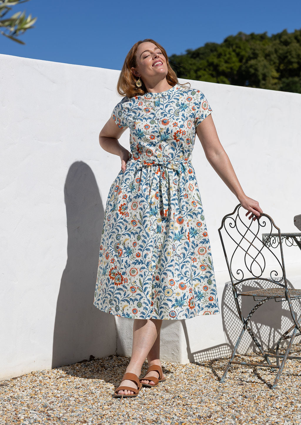 Woman wears retro style cotton button through midi length dress with high round neckline, short sleeves and a removable waist tie.