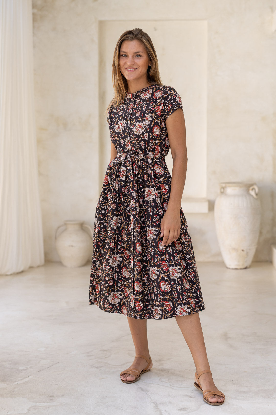 Woman wears retro style cotton button through midi length dress with high round neckline, short sleeves and a removable waist tie.