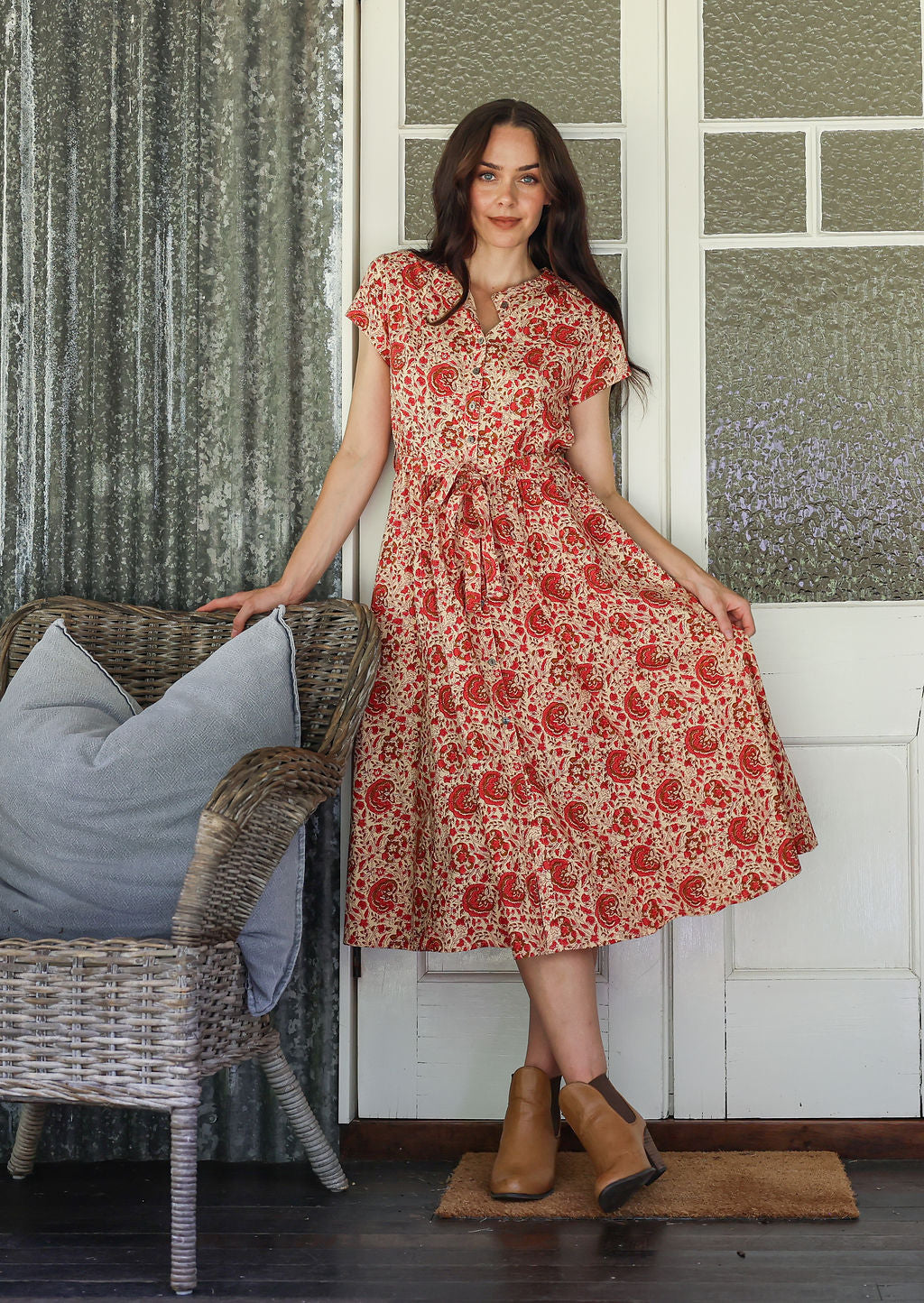 Woman wearing a gentle cream based floral printed cotton button through cotton dress with hidden side pockets, short sleeves and a detachable waist tie.