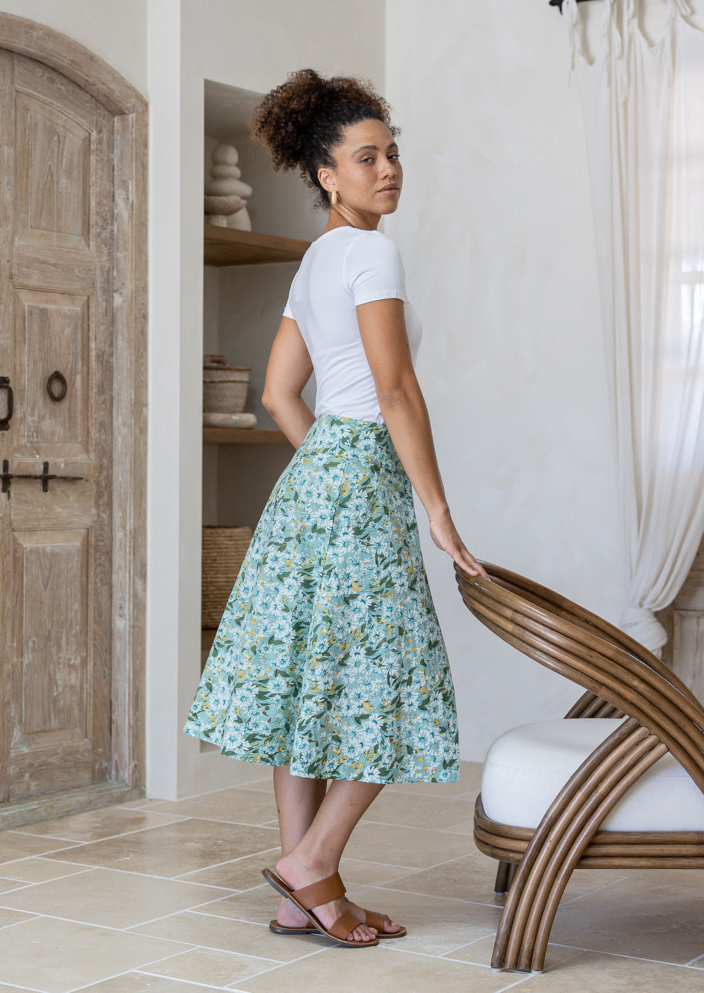 Woman standing sideways wearing a white top and sage green floral cotton skirt in a home setting