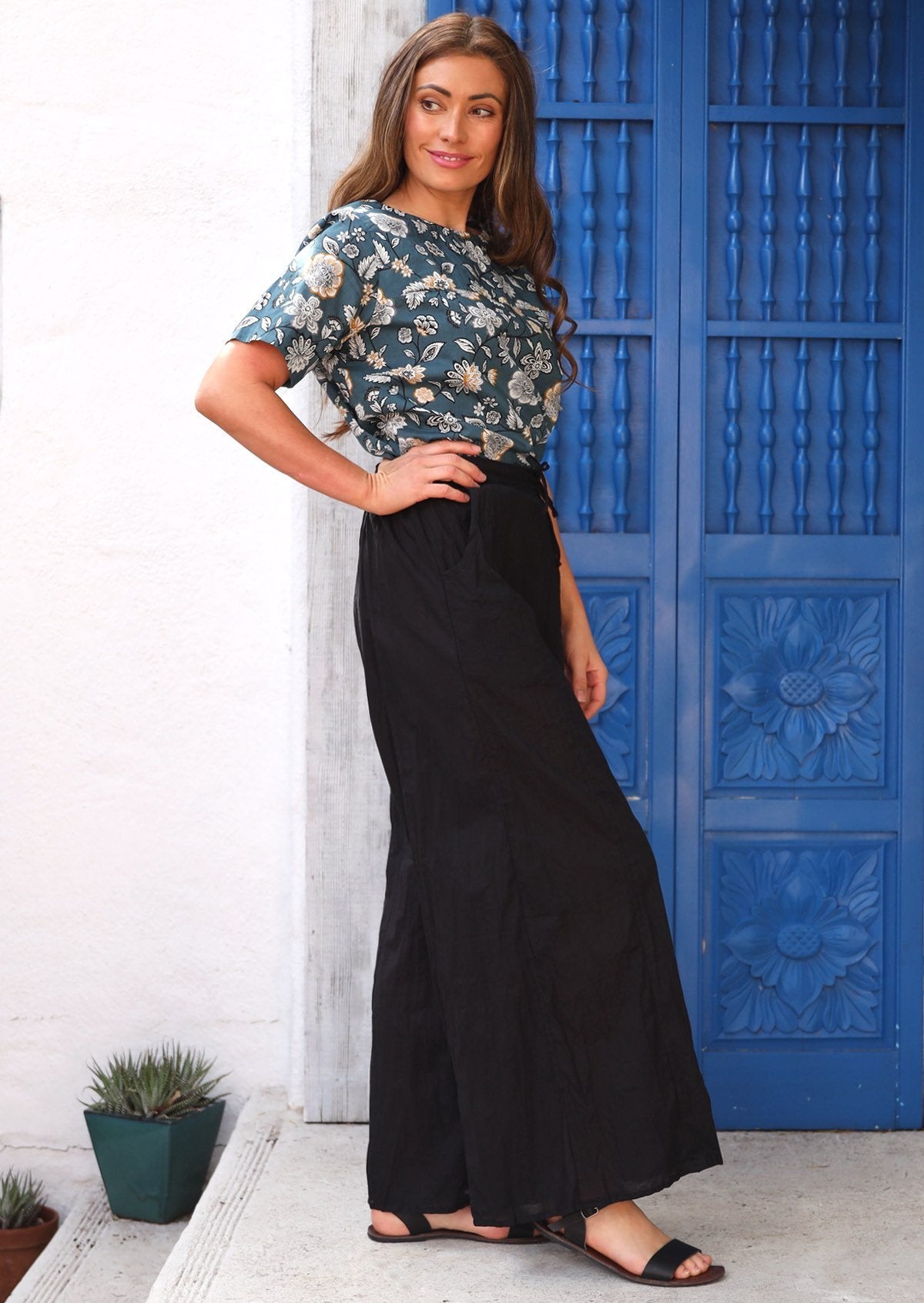 Woman wears 100% light weight cotton pants in black paired with a blue floral top