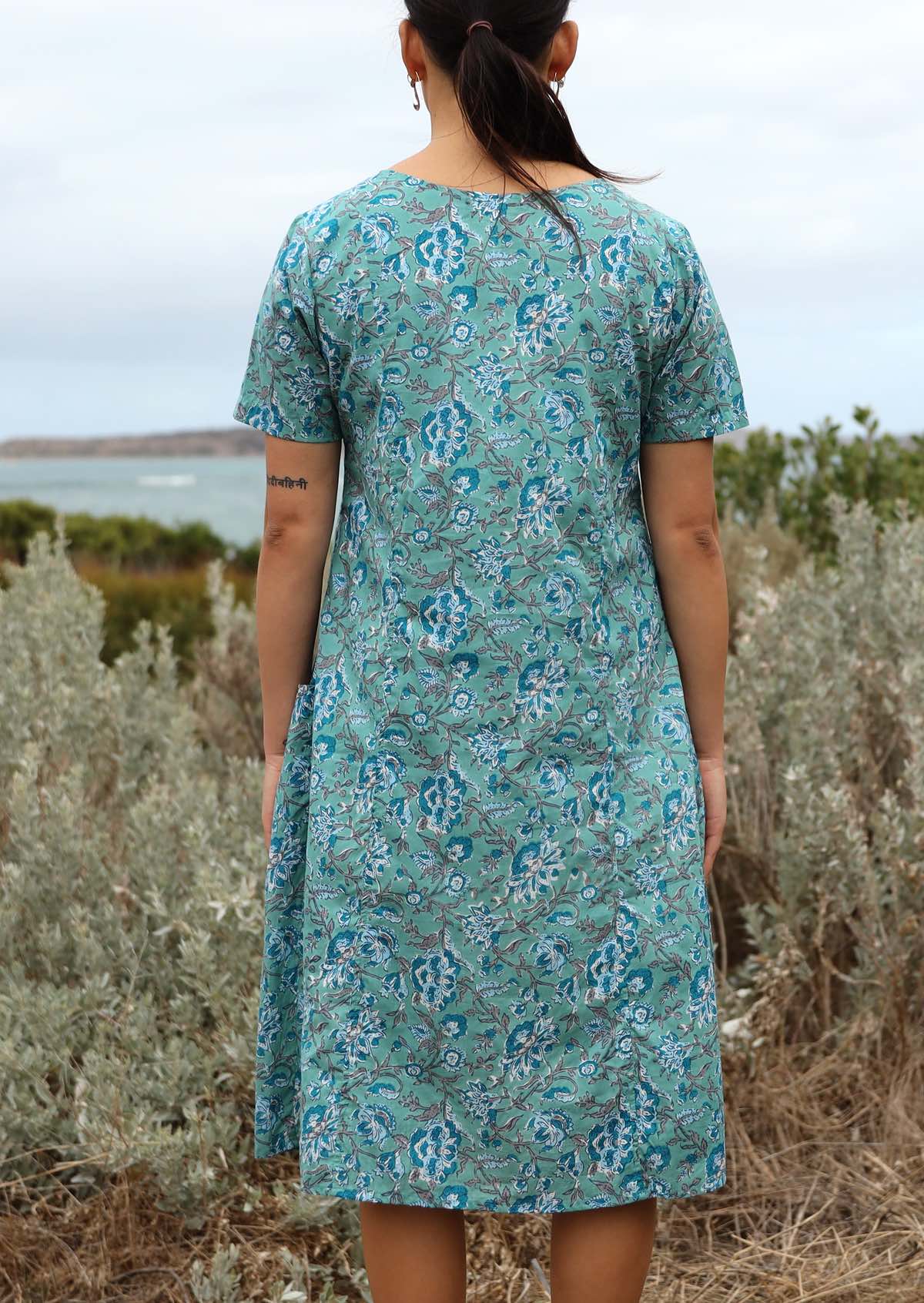 Model standing back wearing mid length cotton dress with relaxed fit and and deep pockets.