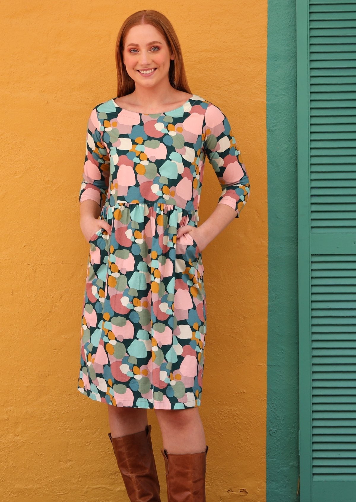 Model wears knee length cotton dress with 3/4 sleeves in pastel print, with hands in pockets