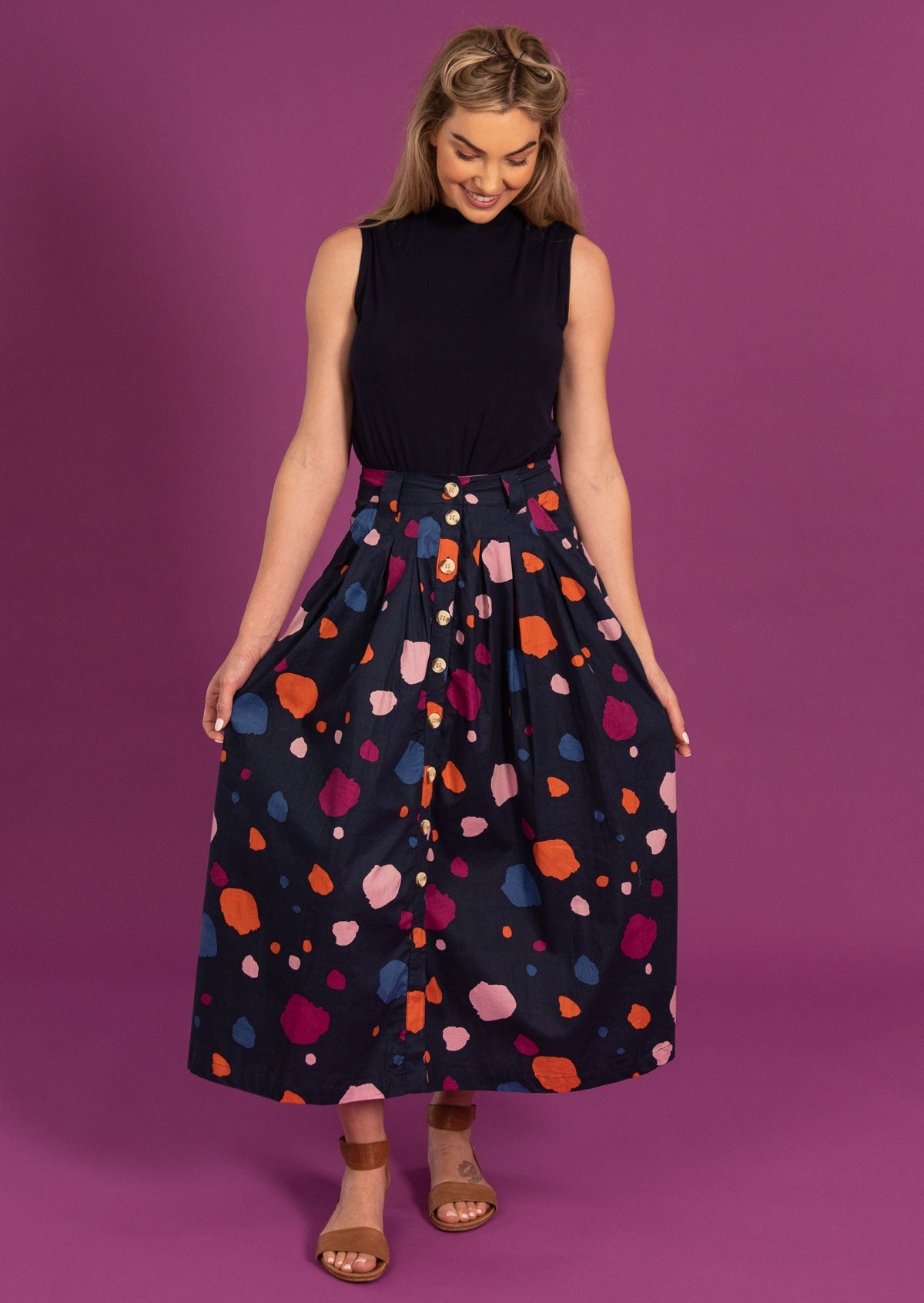 Model poses in a midi length button through skirt with belt loops and box pleats.