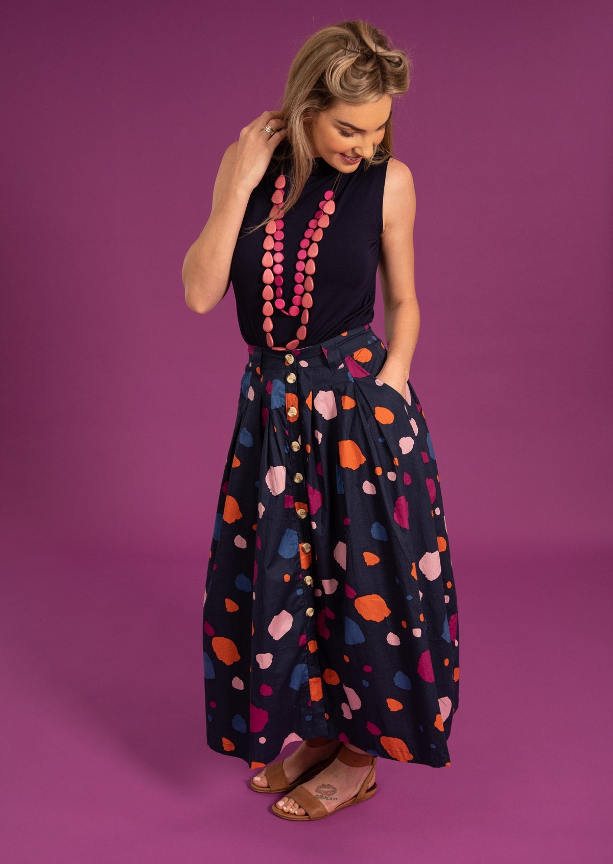 Model standing in front of plum background wears button through cotton skirt in navy blue