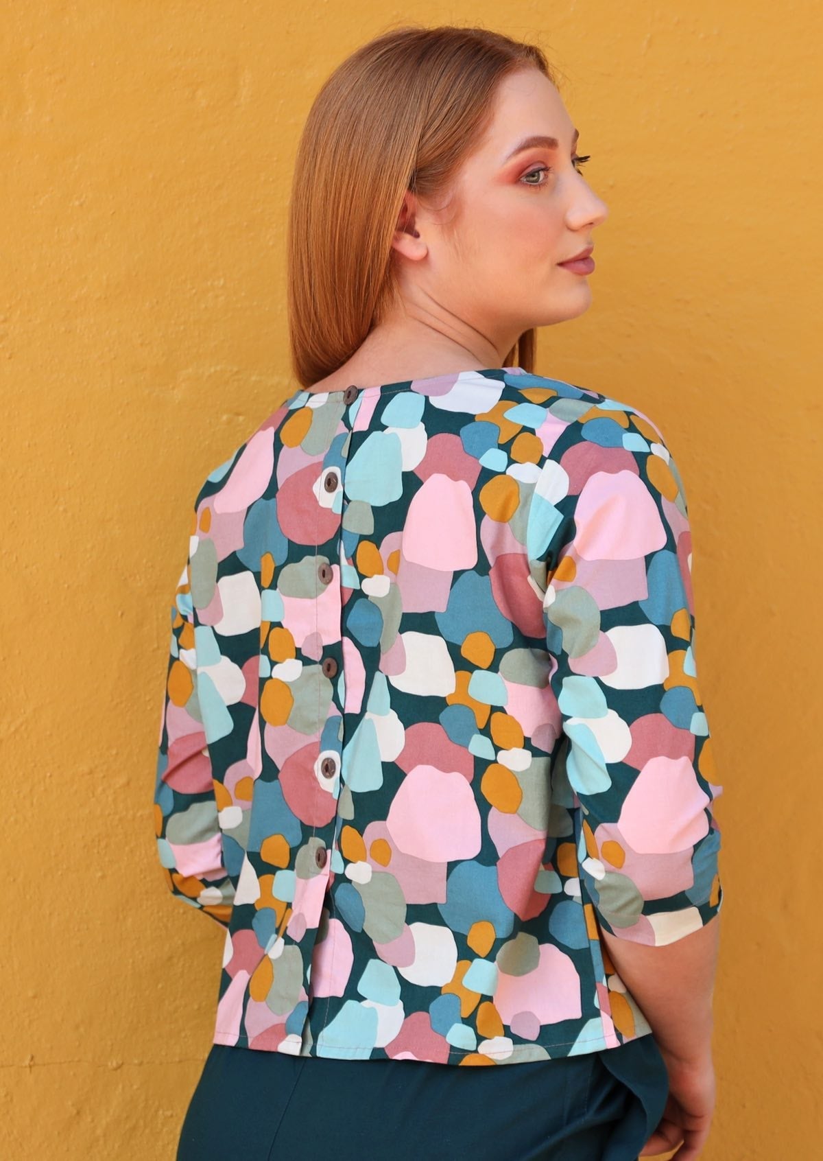 Back view of woman in cotton 3/4 sleeve top with decorative buttons down the centre back