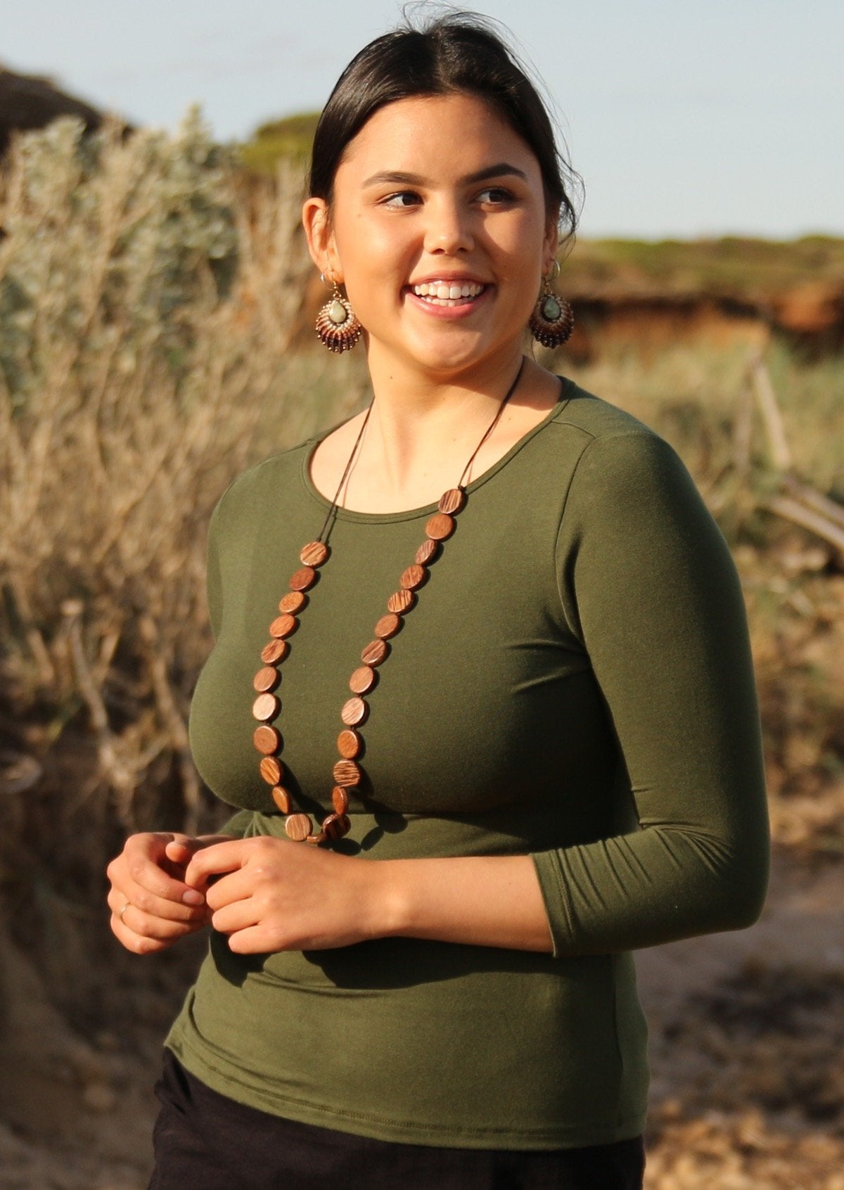 Woman wearing a rayon boat neck olive green 3/4 sleeve top with wooden beads.