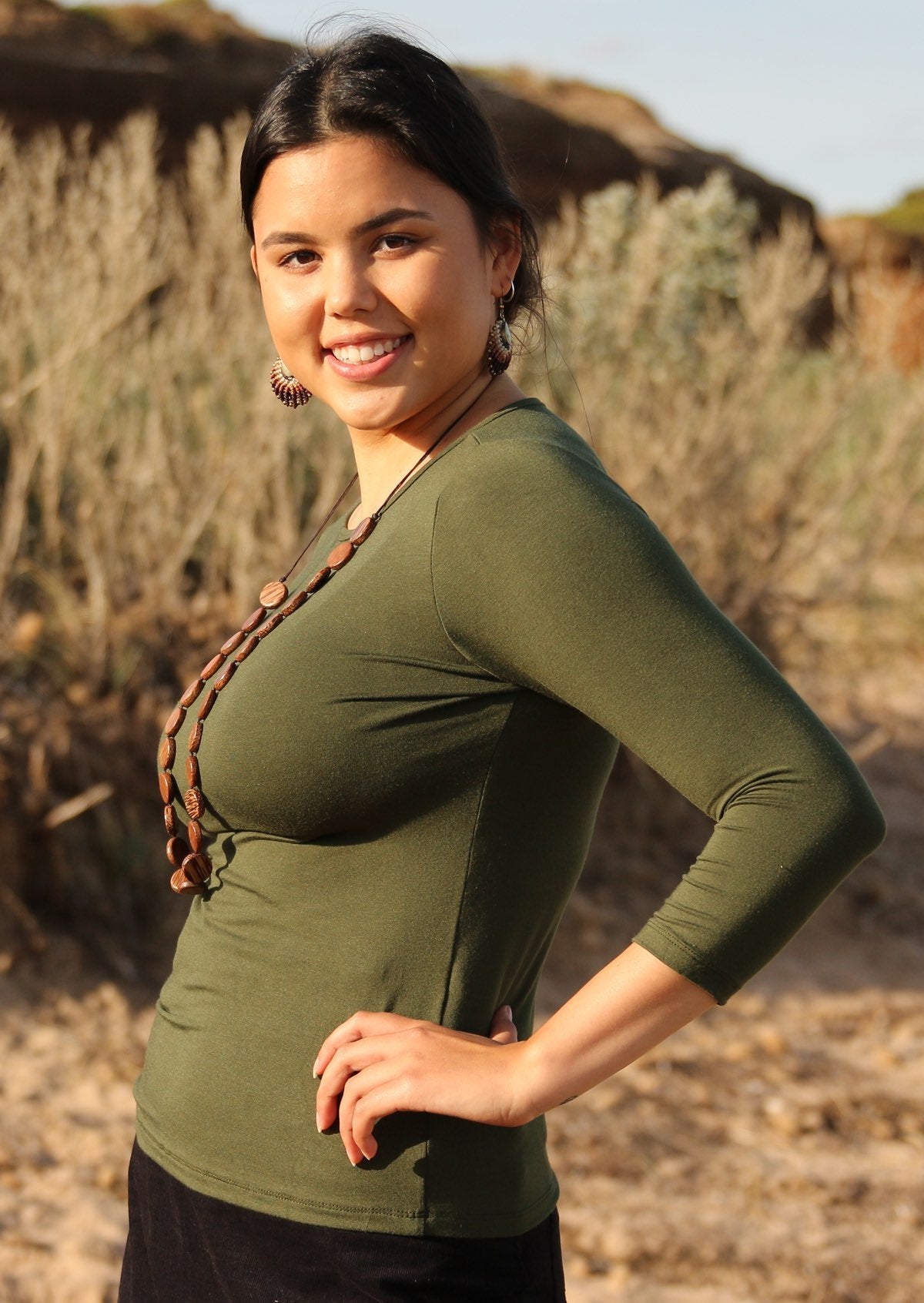 Side view of woman wearing a rayon boat neck olive green 3/4 sleeve top.