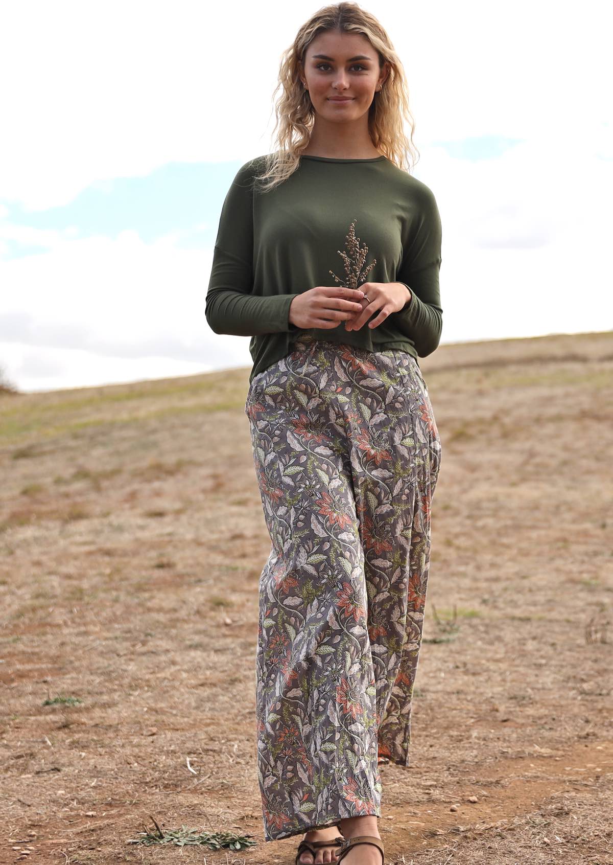 Woman wears cotton wide leg pants with taupe based floral print, paired with an olive green top