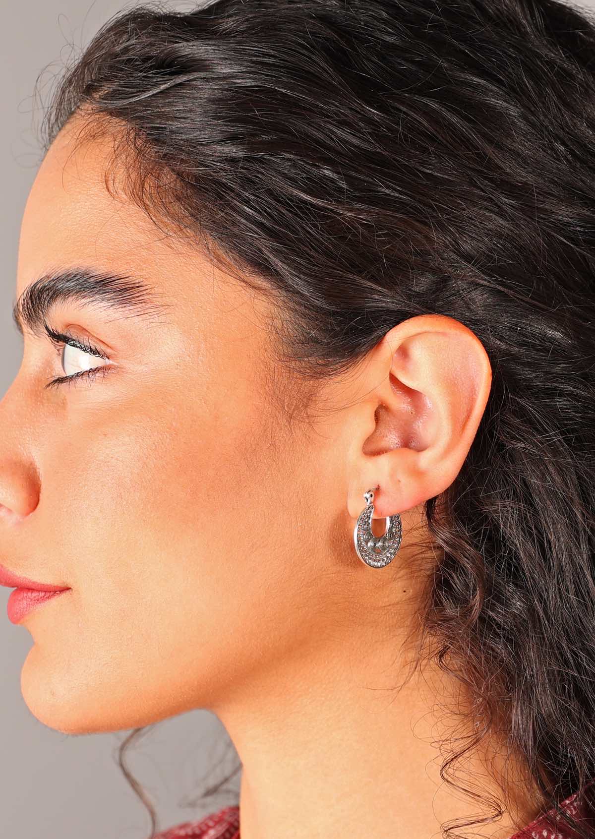 Woman wears silver 20mm diameter fine detailed earring with hinged clasp