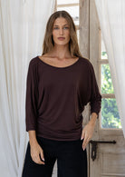 Woman wearing a brown rayon jersey batwing top with 3/4 sleeves and a wide round neckline, paired with black pants