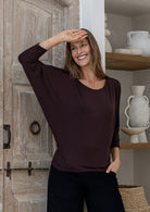 Woman wearing a brown rayon jersey batwing top and black pants, with hand to forehead