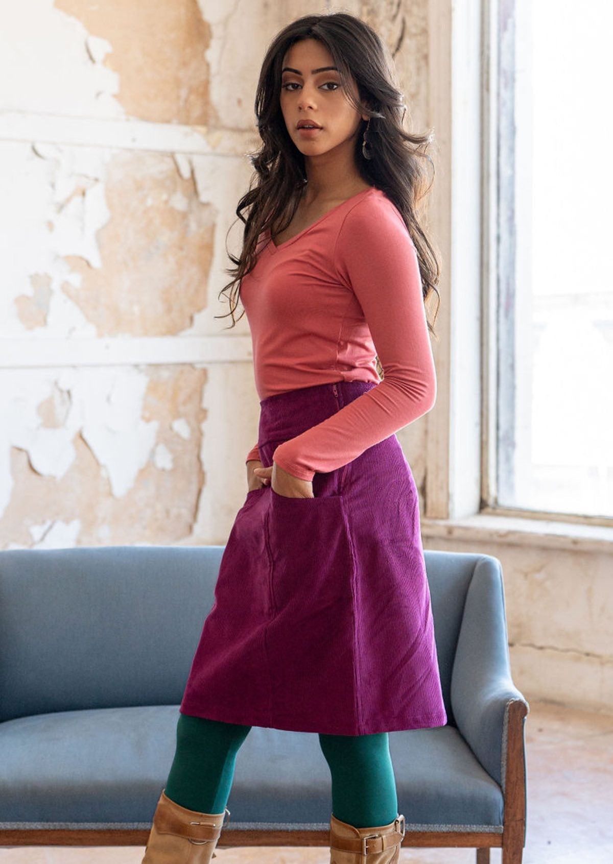 Model poses in plum purple corduroy knee length skirt with side zip and her hands in pockets