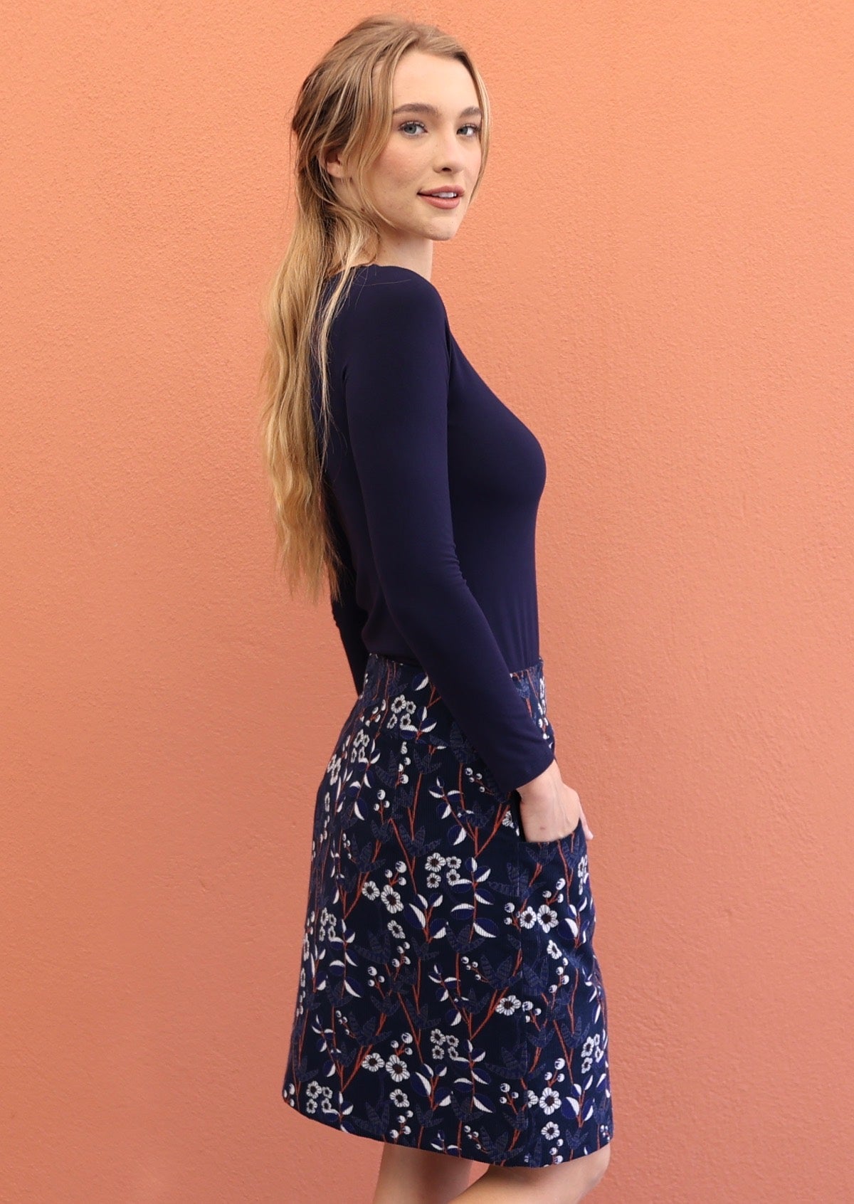 model wearing a mid length skirt featuring  a meadow flower print with blue, white and orange on a navy blue base.