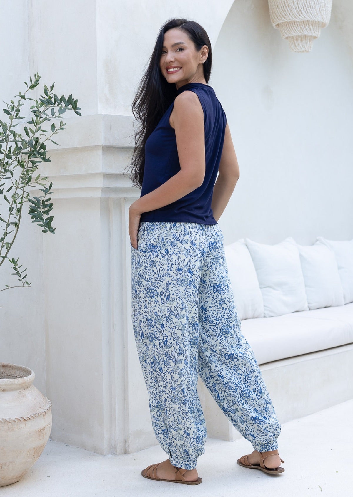 Woman wearing a blue sleeveless top and white and blue floral cotton pants standing in a bright, minimalistic room.