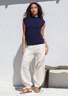Woman wearing a navy top paired with genie style white cotton pants featuring deep pockets, a wide flat front waist and elastic at the back