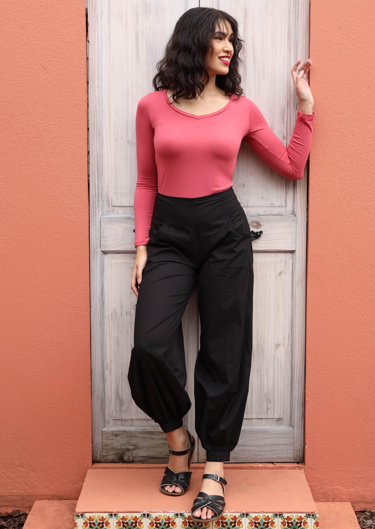 Woman wearing Acapulco Pants shirring across the back, front wide flat waist band wide leg cuffed at ankle with button closure pockets 100% cotton black